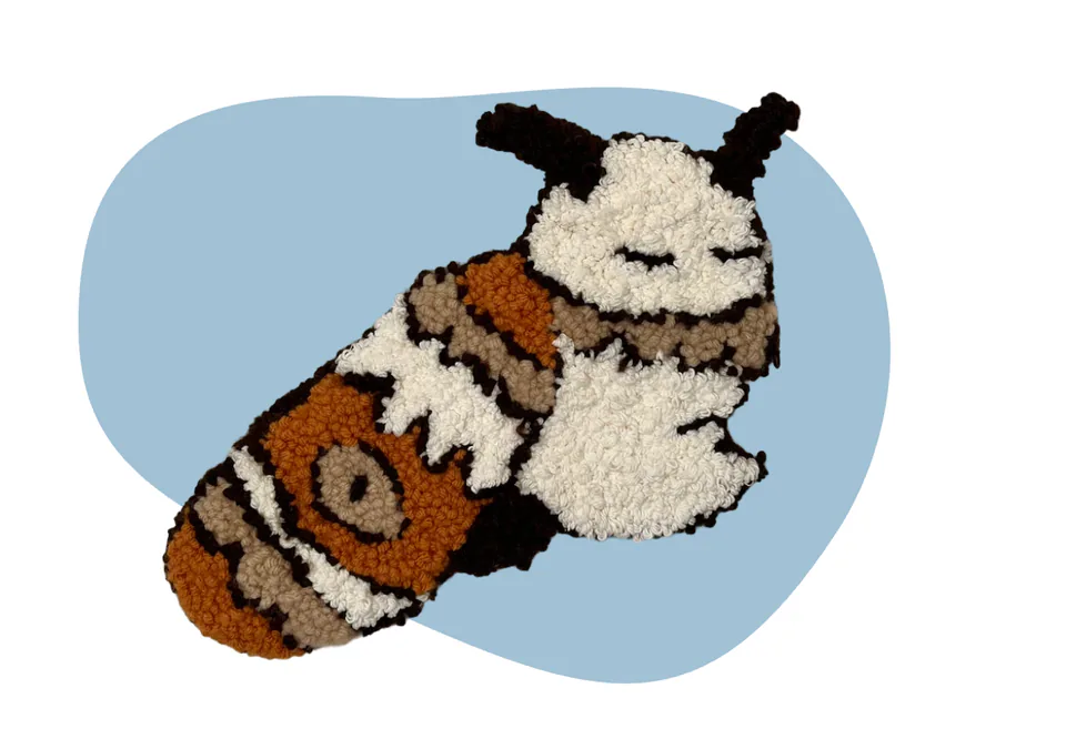 A punch-needle textile moth with tufted cream, brown and black wings, on a pale blue backdrop.