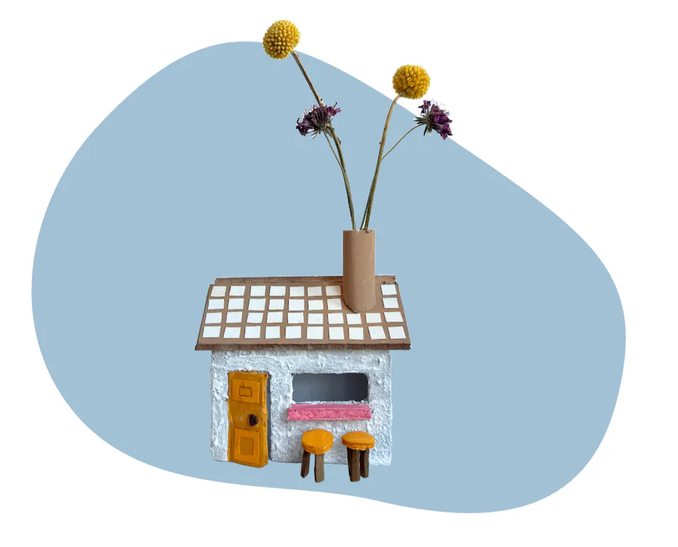 A miniature table holding a tiny vase of dried flowers and a few small objects, on a pale blue backdrop.