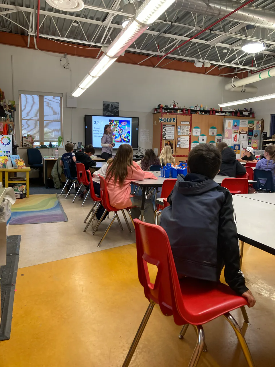 An elementary art room with children working at low tables, finished artwork pinned along the walls.