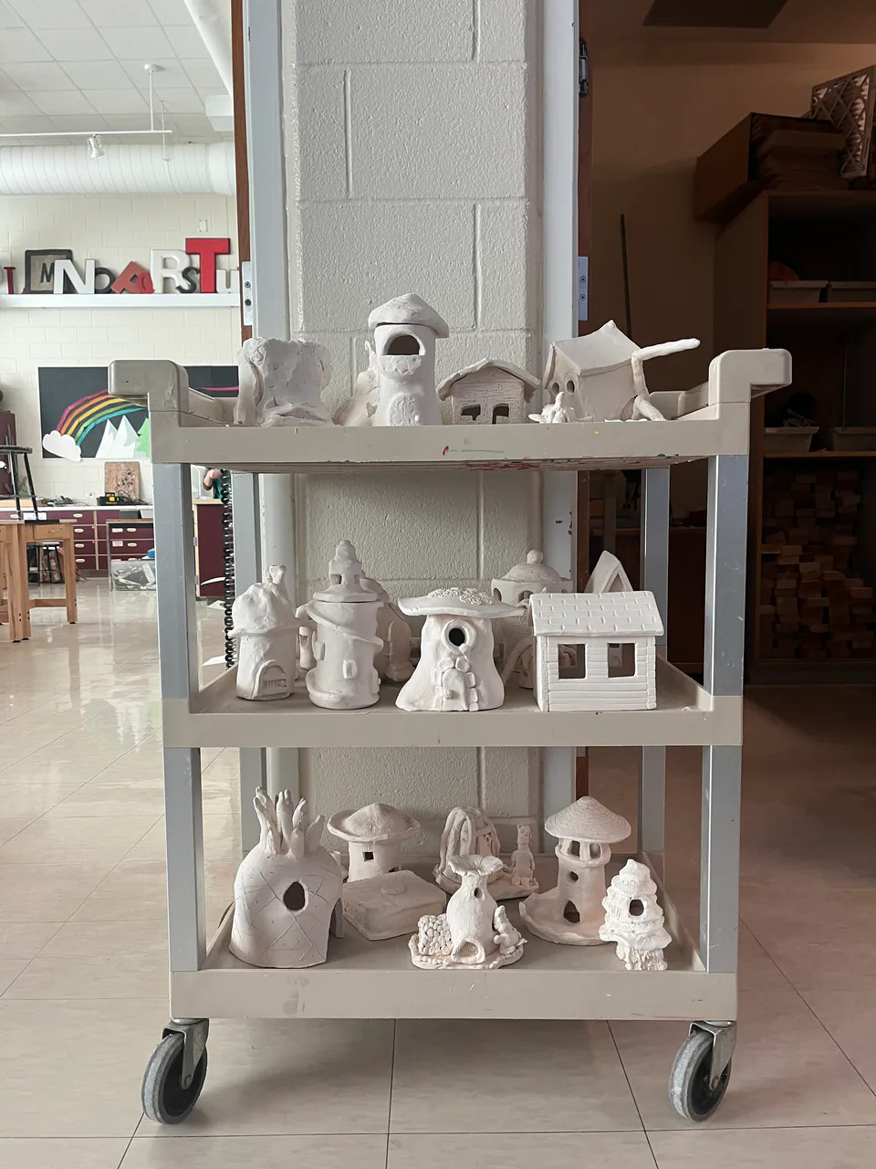 A rolling cart of unglazed white ceramic pieces drying in the art room.
