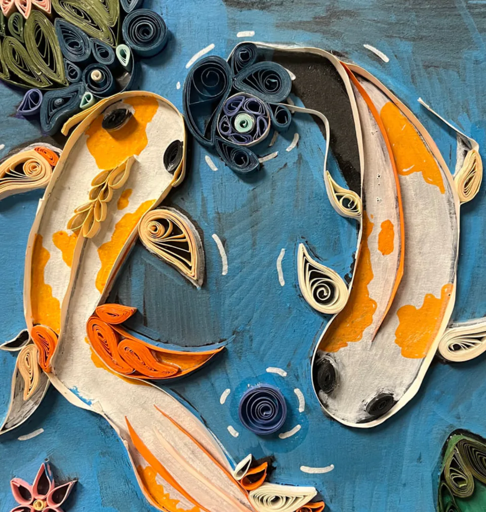 Paper quilling: two orange koi fish swimming among coiled blue water.